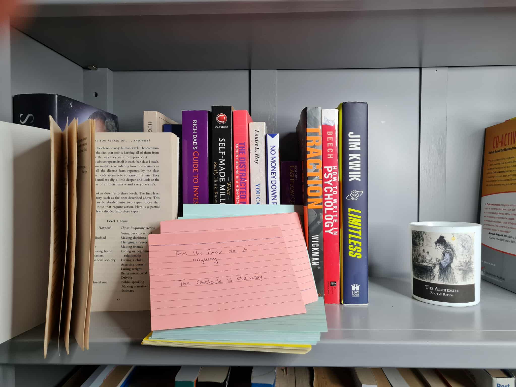 Organized bookshelf with diverse reading collection and handwritten notes about obstacles and fear, representing daily reading habits and everyday mastery principles