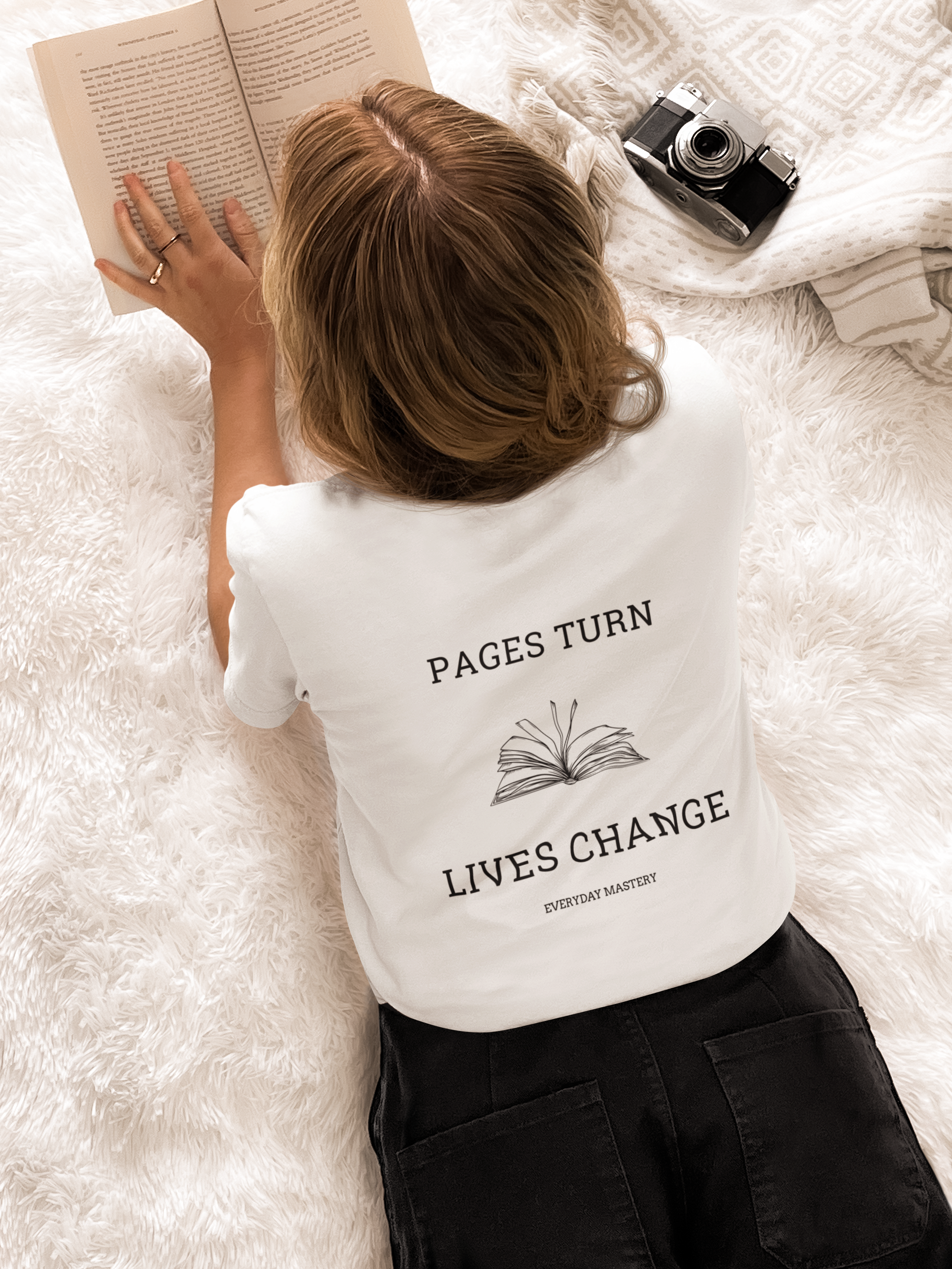 Person reading book while wearing Pages Turn Lives Change everyday mastery t-shirt, demonstrating daily reading habits and personal growth mindset