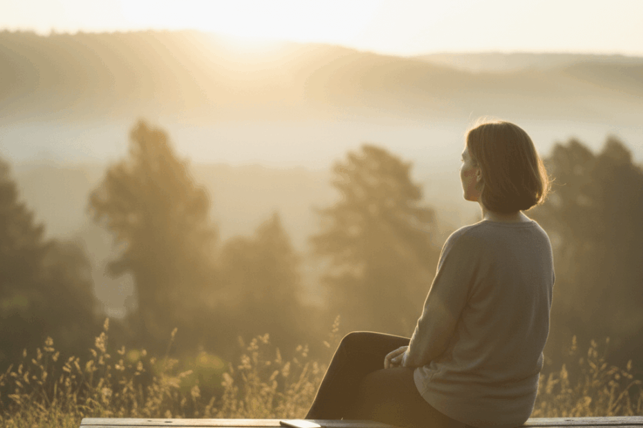 A person sitting on a wooden bench at sunrise, phone placed beside them, gazing quietly at the horizon — symbolising mindful disconnection and the calm clarity of a digital detox.