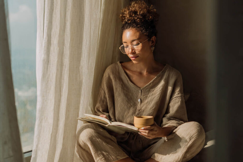 Calm person journaling by a sunlit window with a cup of tea, wearing neutral tones, symbolising peace, reflection, and journaling for overthinking