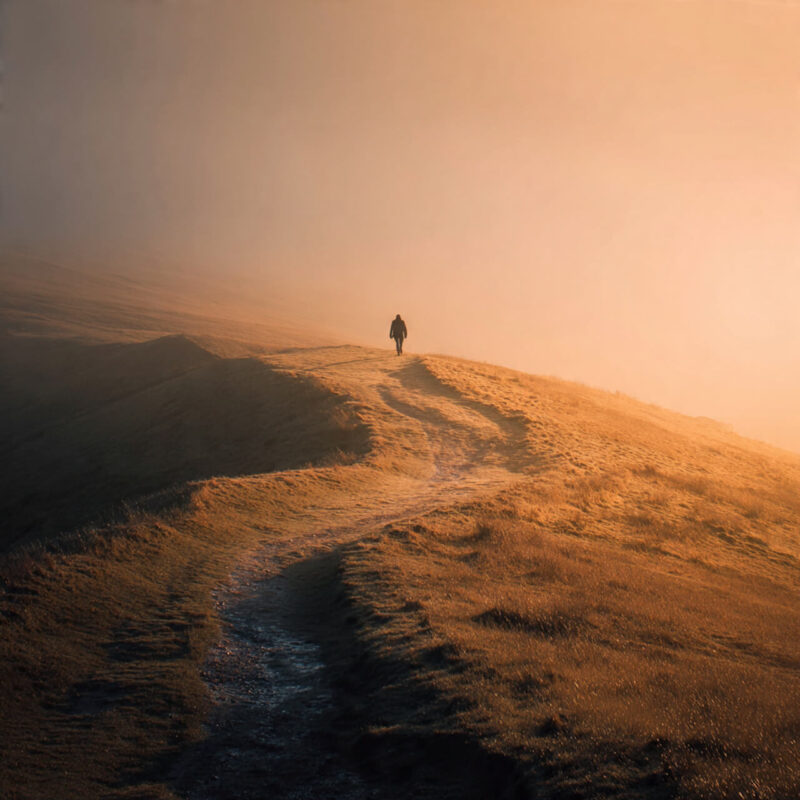 A lone figure walking along a misty hillside at sunrise, warm golden light symbolising perseverance and learning to keep going when no one’s watching.”