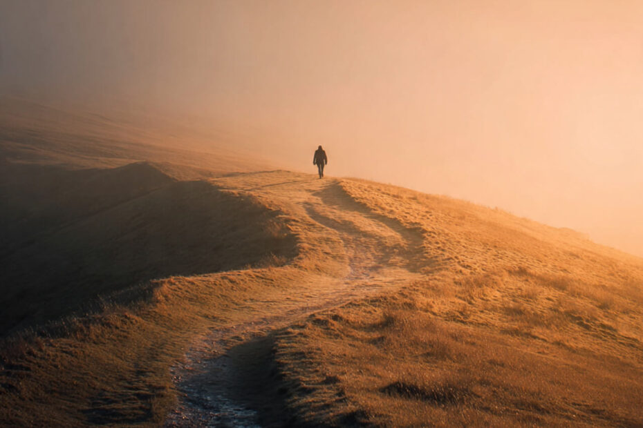 A lone figure walking along a misty hillside at sunrise, warm golden light symbolising perseverance and learning to keep going when no one’s watching.”