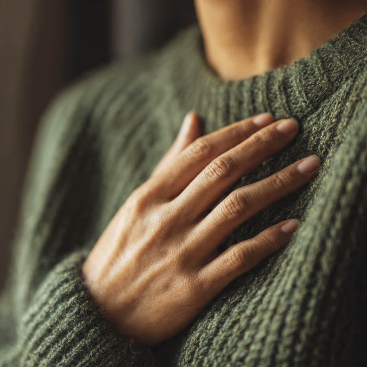 Hand resting gently on chest in a green jumper, illustrating breath awareness and compassion practice.