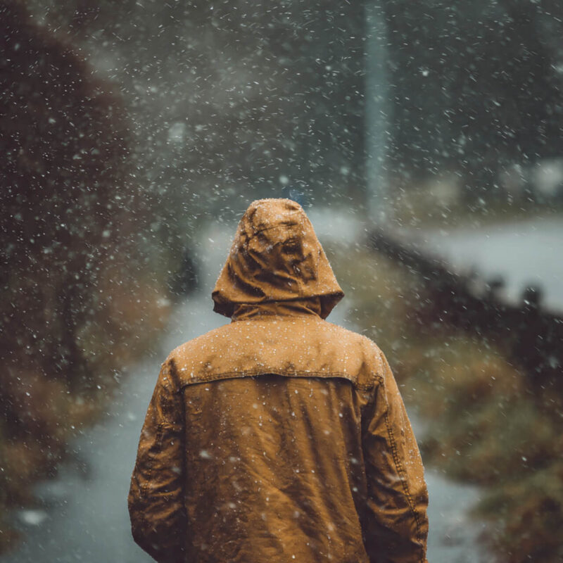 Person walking calmly through light rain wearing a brown coat — illustrating how Stoic resilience is built through patience, presence, and acceptance of discomfort.