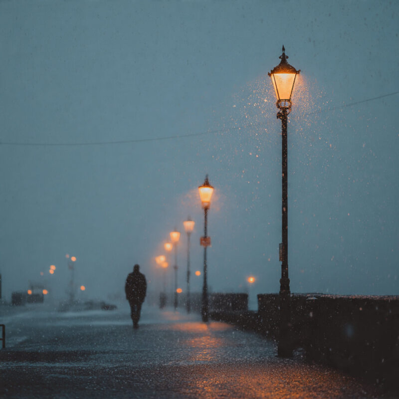 Person walking alone in gentle rain under glowing streetlights in the UK, representing mindfulness and acceptance during dark winter evenings