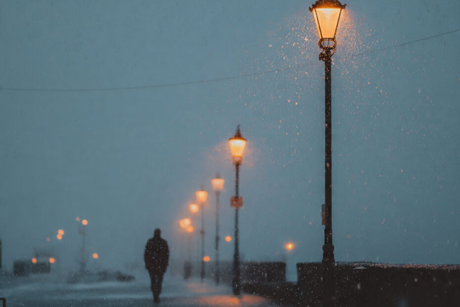 Person walking alone in gentle rain under glowing streetlights in the UK, representing mindfulness and acceptance during dark winter evenings