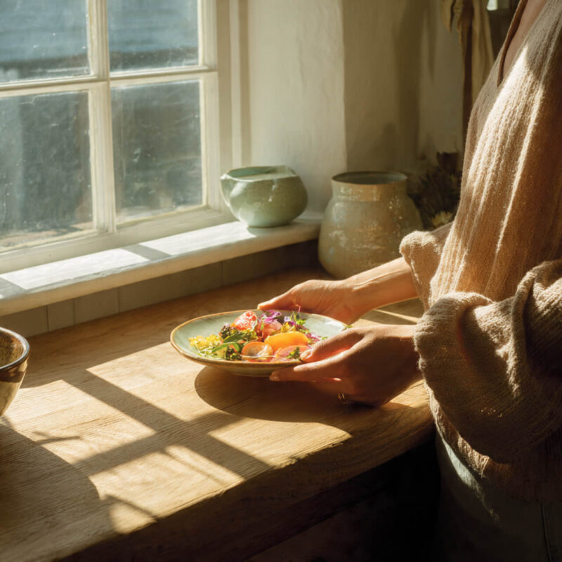Person holding a bowl of colourful whole foods in soft morning light, representing small daily habits for balanced eating and weight loss without willpower.