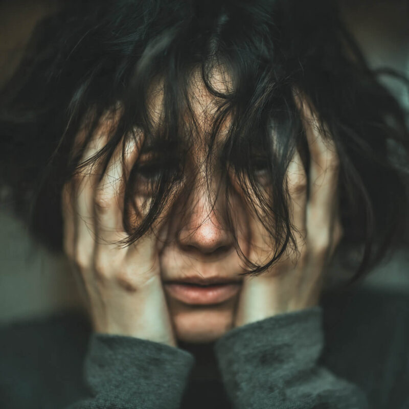 Close-up of a woman holding her face in her hands, conveying emotional overwhelm before learning how to reset her mindset