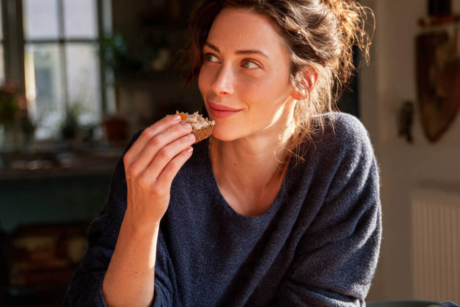 Woman enjoying toast with sauerkraut at a sunlit breakfast table, showing the process of retraining the palate and building sustainable gut health habits
