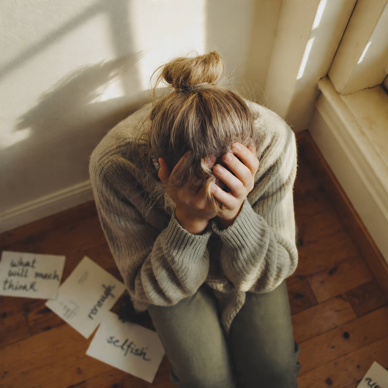 Overwhelmed woman with head in hands surrounded by notes showing burnout from people-pleasing and seeking approval