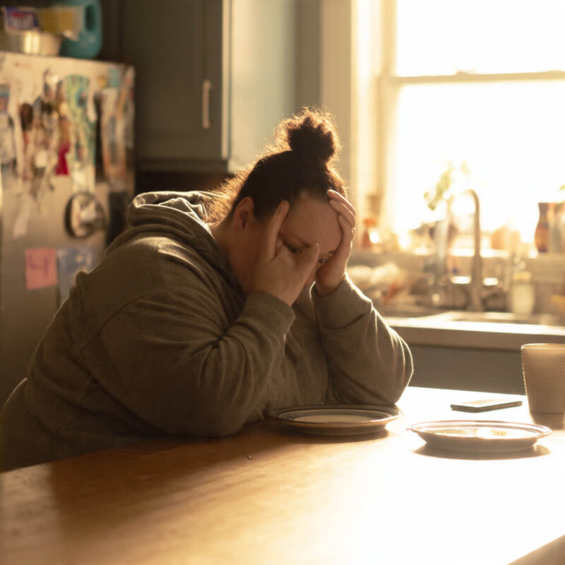 Woman sitting at kitchen table with head in hands feeling overwhelmed by dieting wondering why diets fail