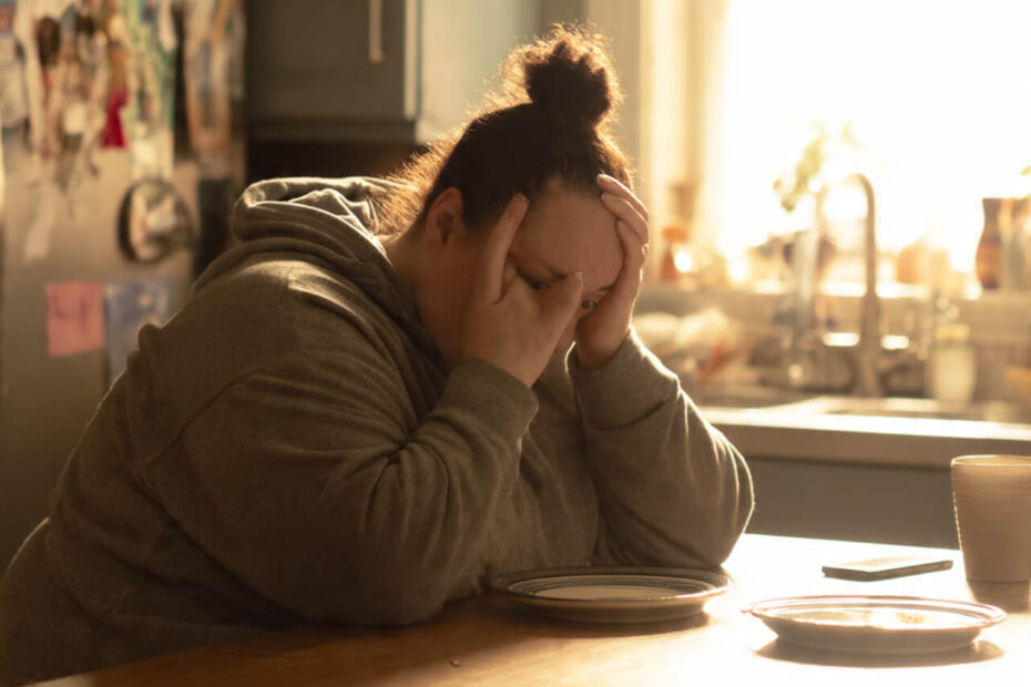 Woman sitting at kitchen table with head in hands feeling overwhelmed by dieting