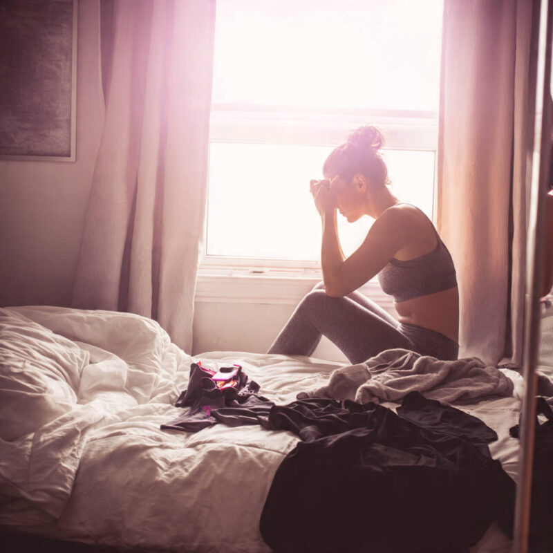 Woman sitting on edge of unmade bed in workout clothes struggling with motivation in early morning light