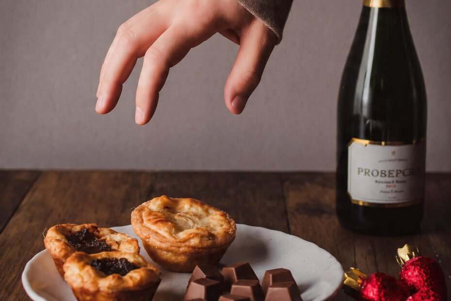 Hand reaching for mince pies and chocolates with prosecco bottle - representing the choice to maintain habits during Christmas celebrations
