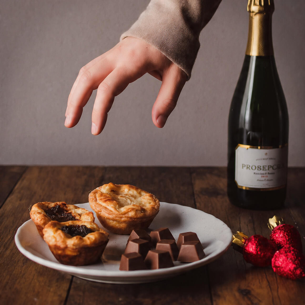 Hand reaching for mince pies and chocolates with prosecco bottle - representing the choice to maintain habits during Christmas celebrations