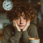 Why Motivation Fails and What Actually Creates Results Close-up of a person resting their face in their hands beside a coffee mug, illustrating decision fatigue and loss of motivation in the evening