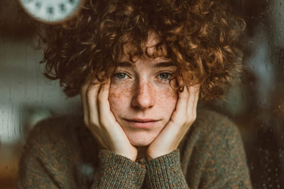 Close-up of a person resting their face in their hands beside a coffee mug, illustrating decision fatigue and loss of motivation in the evening