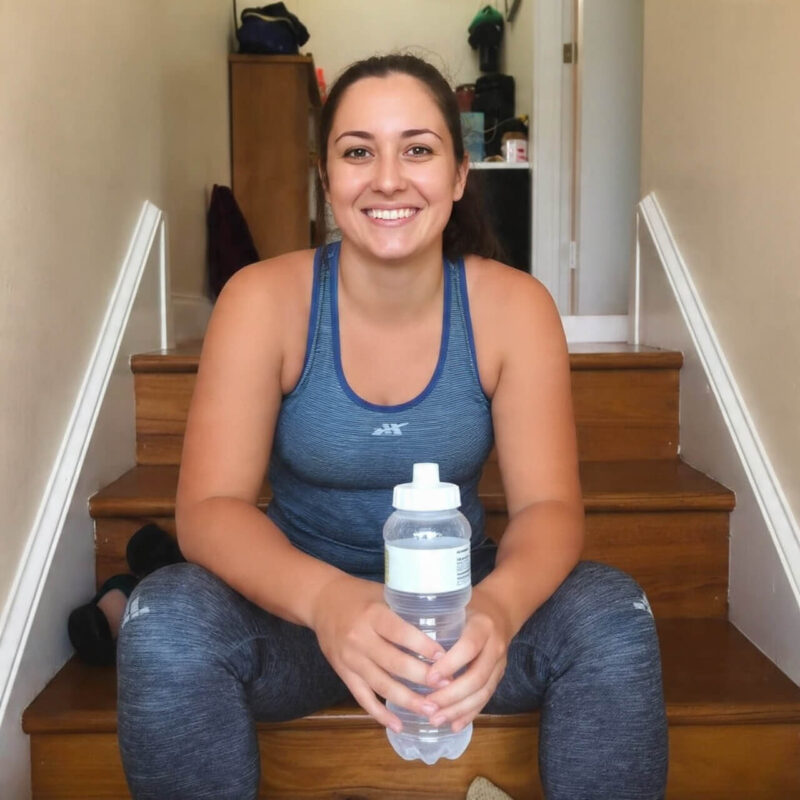 Smiling woman sitting on stairs after completing home workout holding water bottle