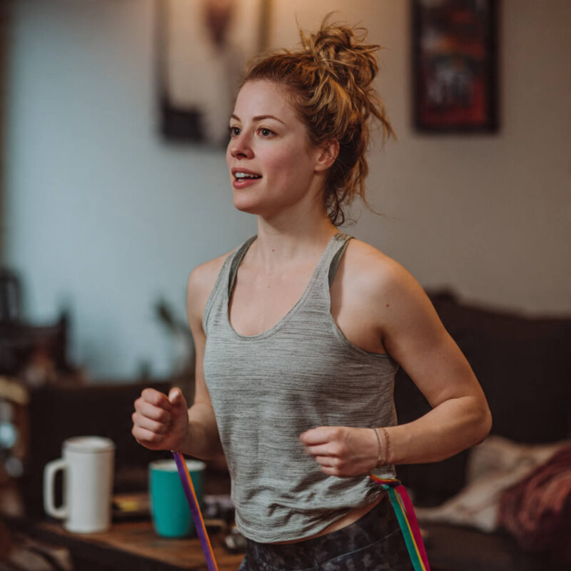 Woman doing home exercise with resistance bands in living room wearing casual workout clothes