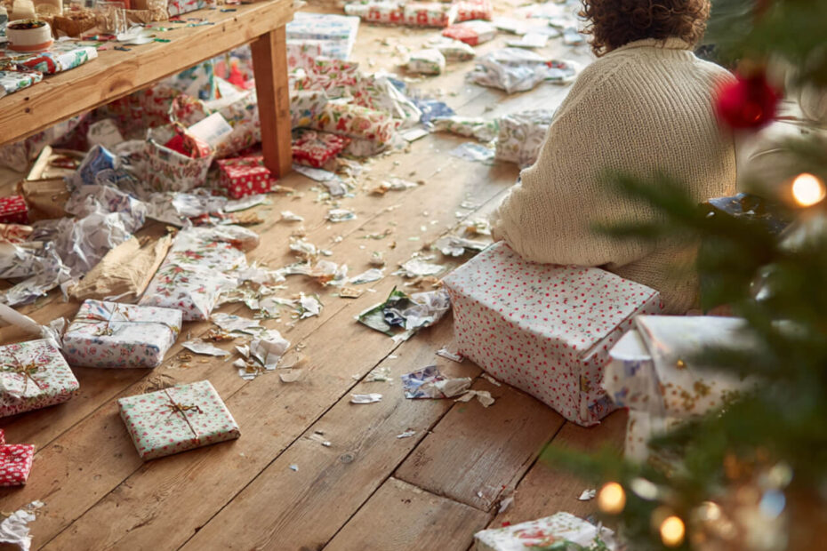 Person in cozy jumper sitting on floor surrounded by Christmas wrapping paper and presents on Christmas morning
