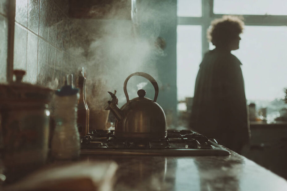 Person staring out kitchen window while kettle boils, lost in thought, going through the motions of their morning routine